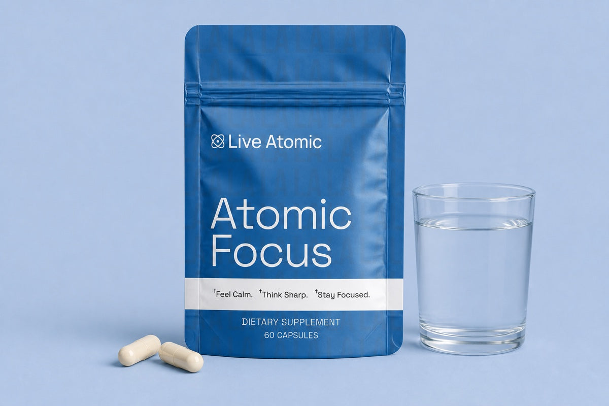 Two Atomic Focus capsules poured into a hand beside a glass of water